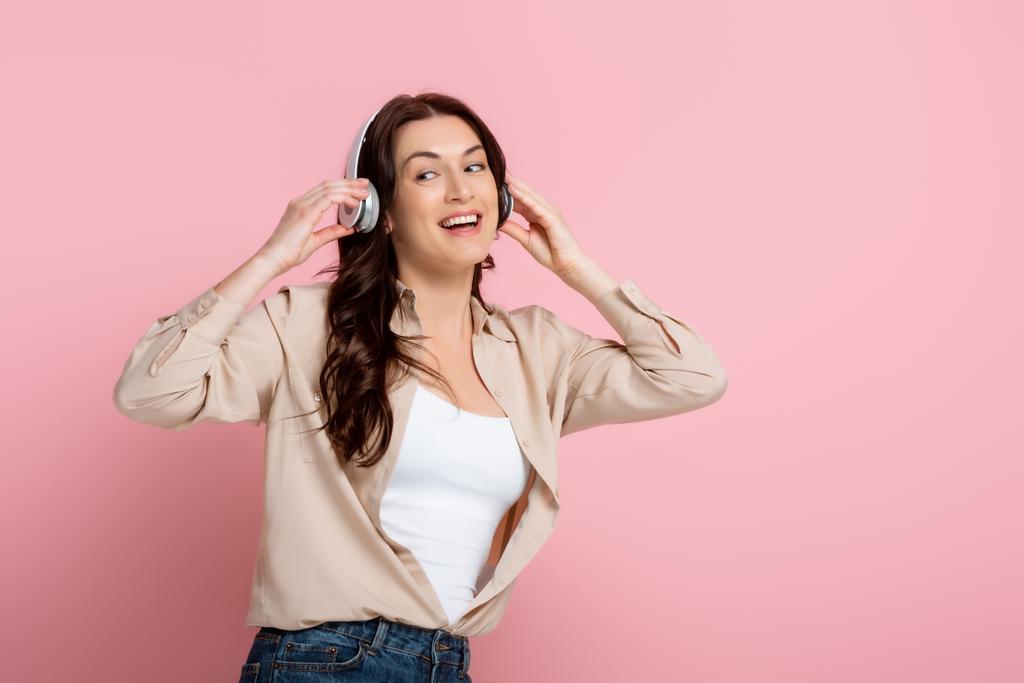 Fröhliche Frau mit Kopfhörern, die auf rosa Hintergrund wegschaut - Foto, Bild