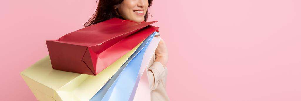 Panoramic crop of smiling woman holding shopping bags isolated on pink - Photo, Image