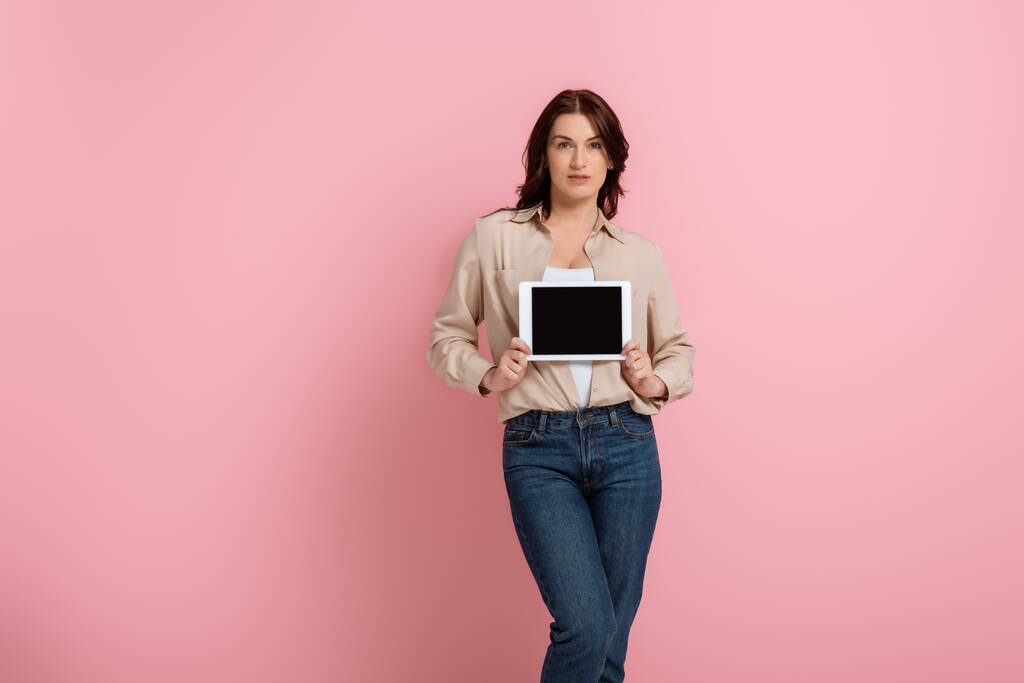 Приваблива брюнетка жінка тримає цифровий планшет з порожнім екраном на рожевому фоні, концепція позитивного тіла
  - Фото, зображення