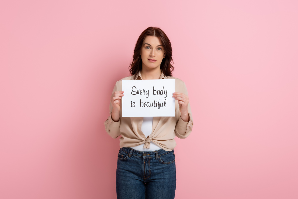 Beautiful woman holding card with every body is beautiful lettering on pink background - Photo, Image