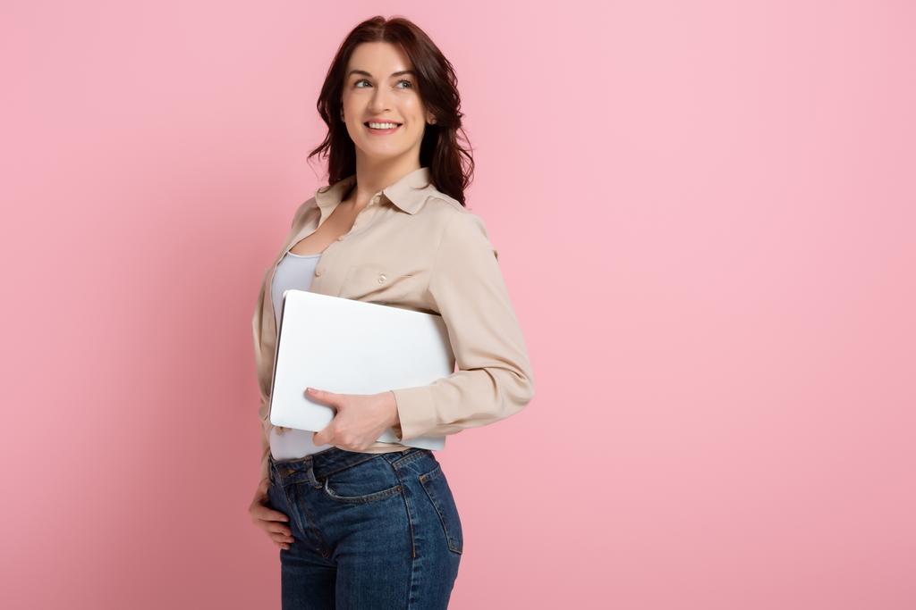 ピンクの背景にノートパソコンを持ちながら笑顔で笑顔を見せるポジティブ女性、体のコンセプト - 写真・画像