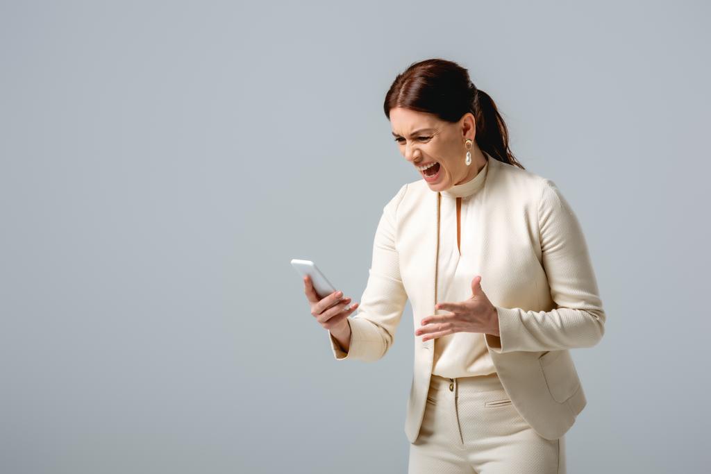 Сердита бізнес-леді кричить, тримаючи смартфон ізольовано на сірому
  - Фото, зображення