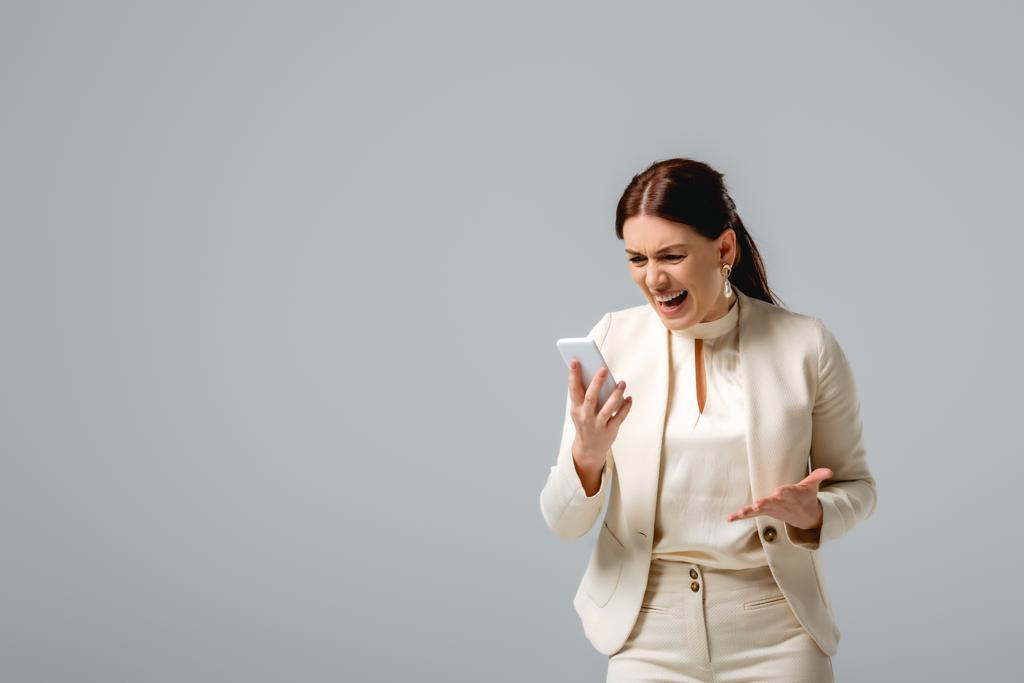 Επιθετική επιχειρηματίας ουρλιάζοντας κρατώντας smartphone απομονώνονται σε γκρι  - Φωτογραφία, εικόνα