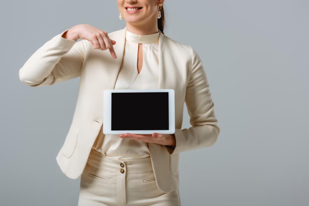 Gri üzerinde izole edilmiş dijital tablete işaret eden gülümseyen iş kadını görüntüsü  - Fotoğraf, Görsel