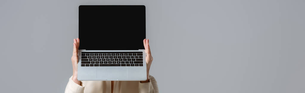 Récolte panoramique d'une femme tenant un ordinateur portable avec écran blanc isolé sur gris  - Photo, image