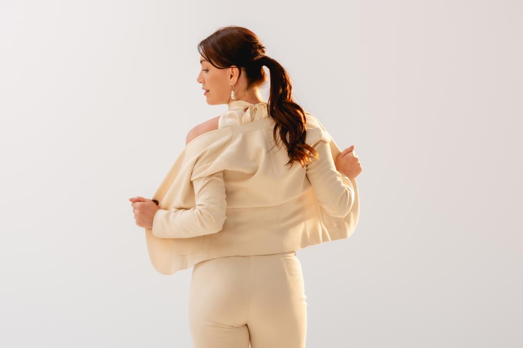 Вид ззаду красива бізнес-леді знімає піджак ізольовано на сірому
  - Фото, зображення