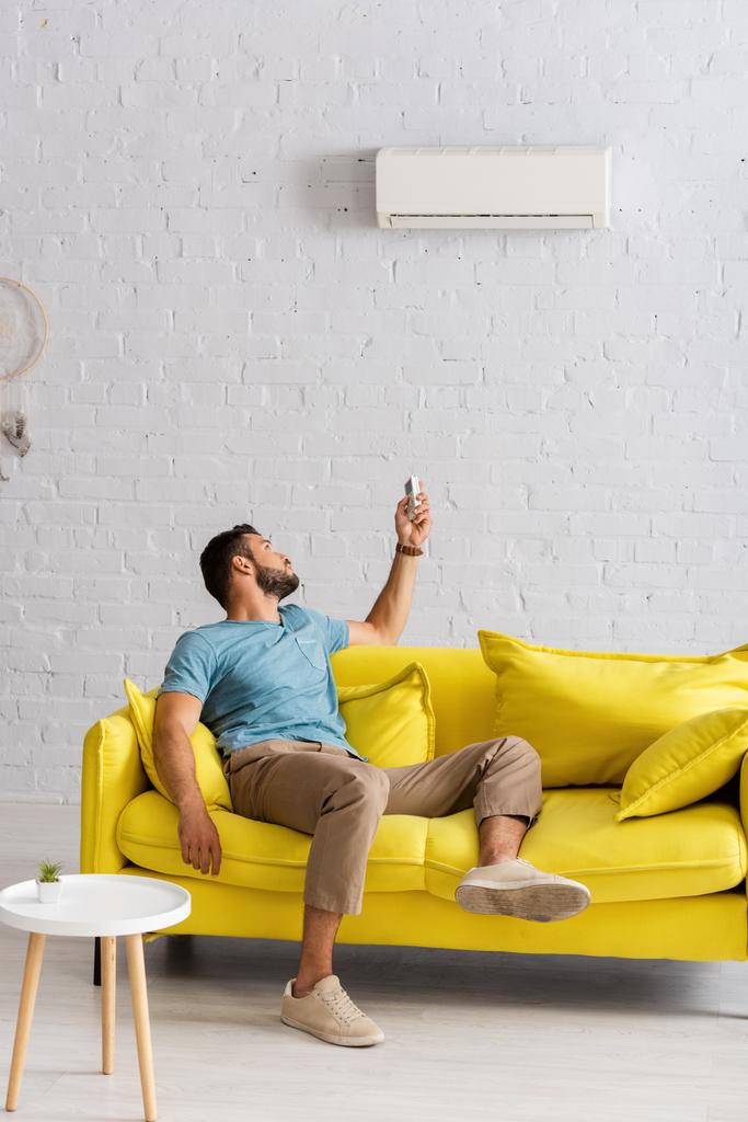 Nuori mies vaihtaa ilmastointilaite kaukosäädin olohuoneessa - Valokuva, kuva