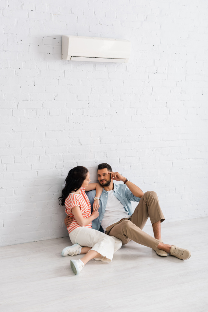 Bonito homem abraçando namorada enquanto sentados juntos no chão sob ar condicionado
  - Foto, Imagem