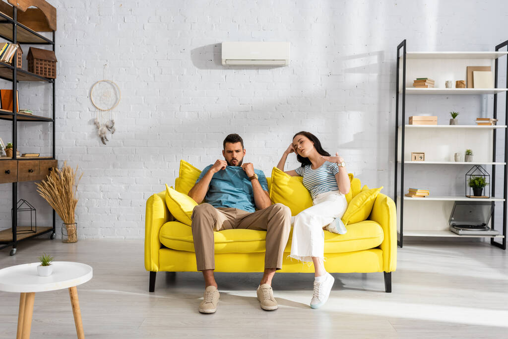 Focus selettivo della giovane coppia esausta che si sente calda sul divano in soggiorno  - Foto, immagini