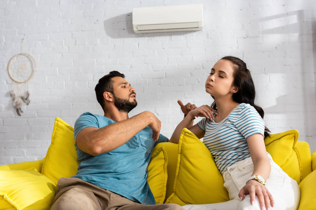 Fešák muž foukání na přítelkyni, zatímco pocit horka v obývacím pokoji - Fotografie, Obrázek