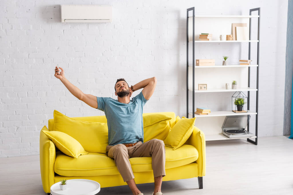 Hombre guapo conmutando aire acondicionado con mando a distancia en la sala de estar
 - Foto, Imagen