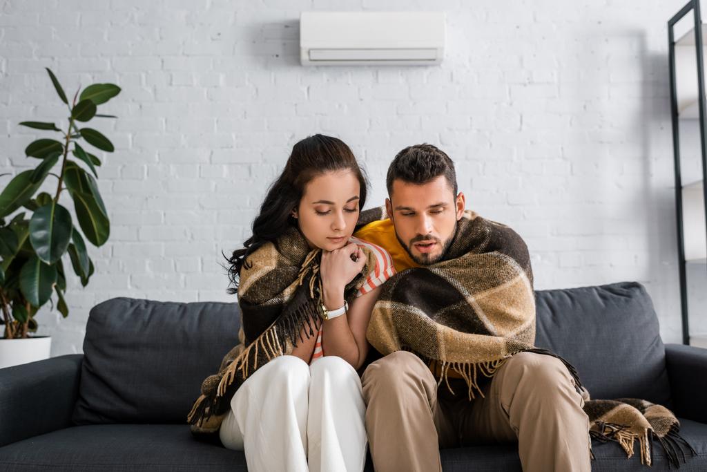 Frozen young couple wrapping in plaid on couch at home  - Photo, Image