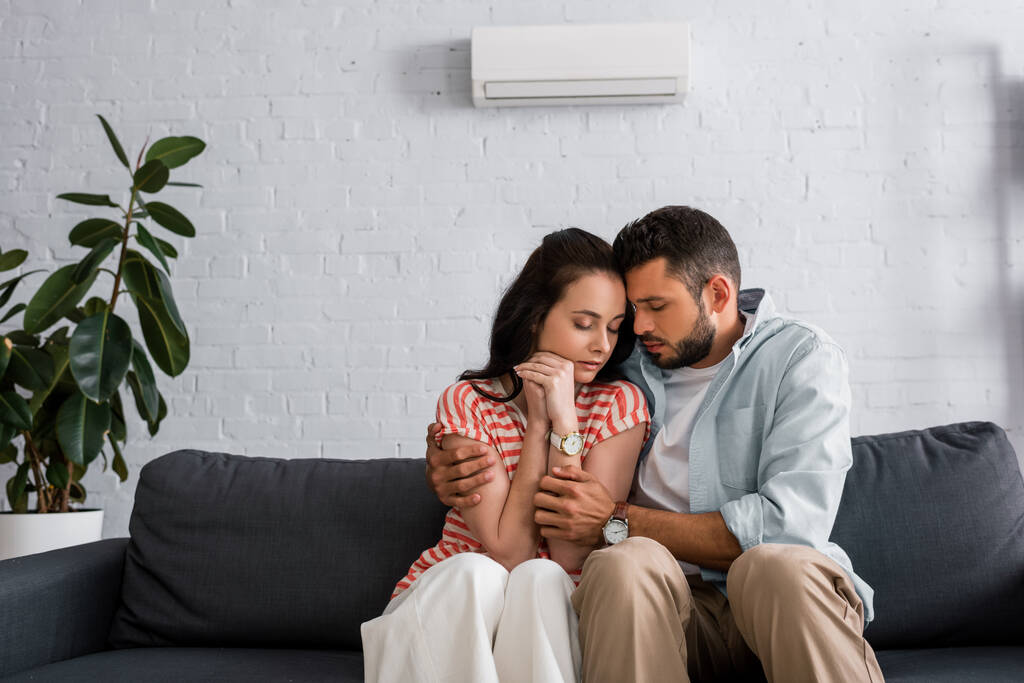Bonito homem abraçando namorada enquanto se sente frio na sala de estar
 - Foto, Imagem