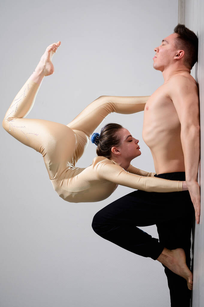 Ένα ντουέτο ακροβάτες που δείχνουν ένα διπλό κόλπο. Μια γυναίκα με φόρμα γυμναστικής πάνω από έναν ημίγυμνο άντρα ξαπλώνει ανάσκελα. Πολύ ευέλικτοι καλλιτέχνες τσίρκου. - Φωτογραφία, εικόνα