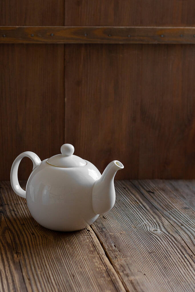 Witte keramische mockup theepot voor warme thee op lege oude houten tafel in de buurt van muur gemaakt van bruin hout planken. Verticale banner met kopieerruimte. Rustieke stijl. - Foto, afbeelding