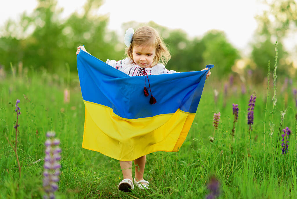 Dziecko nosi trzepoczącą flagę Ukrainy na polu. Dzień Niepodległości Ukrainy. Dzień Flagi. Dzień Konstytucji. Dziewczyna w tradycyjnym hafcie z flagą Ukrainy - Zdjęcie, obraz