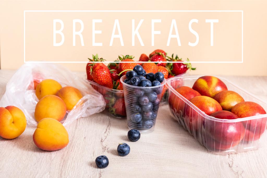 bosbessen, aardbeien, nectarines en perziken in plastic containers op houten ondergrond bij het ontbijt belettering op beige - Foto, afbeelding