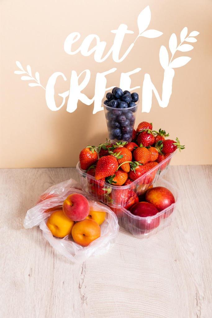 ブルーベリー、イチゴ、ネクタリン、桃をプラスチック容器に入れた果物の組成物はベージュで緑の文字を食べる  - 写真・画像