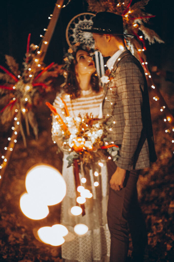 Κομψό ζευγάρι νυφών σε μια γαμήλια φωτογράφηση στο πάρκο το βράδυ με λαμπερά φώτα και λαμπιόνια - Φωτογραφία, εικόνα