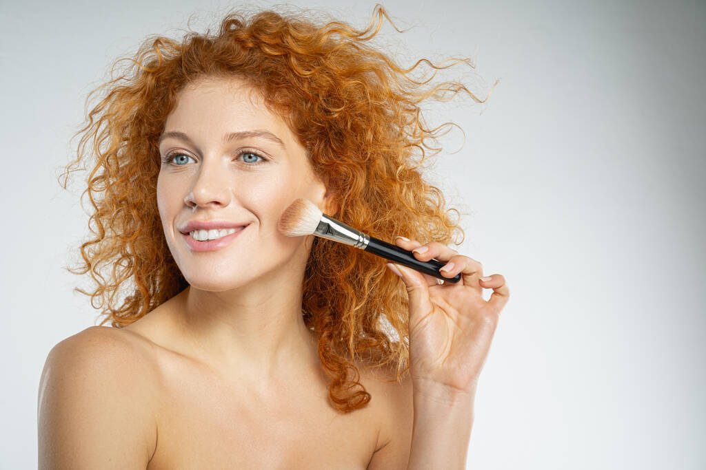 Wesoła kręcona kobieta robi naturalny makijaż - Zdjęcie, obraz
