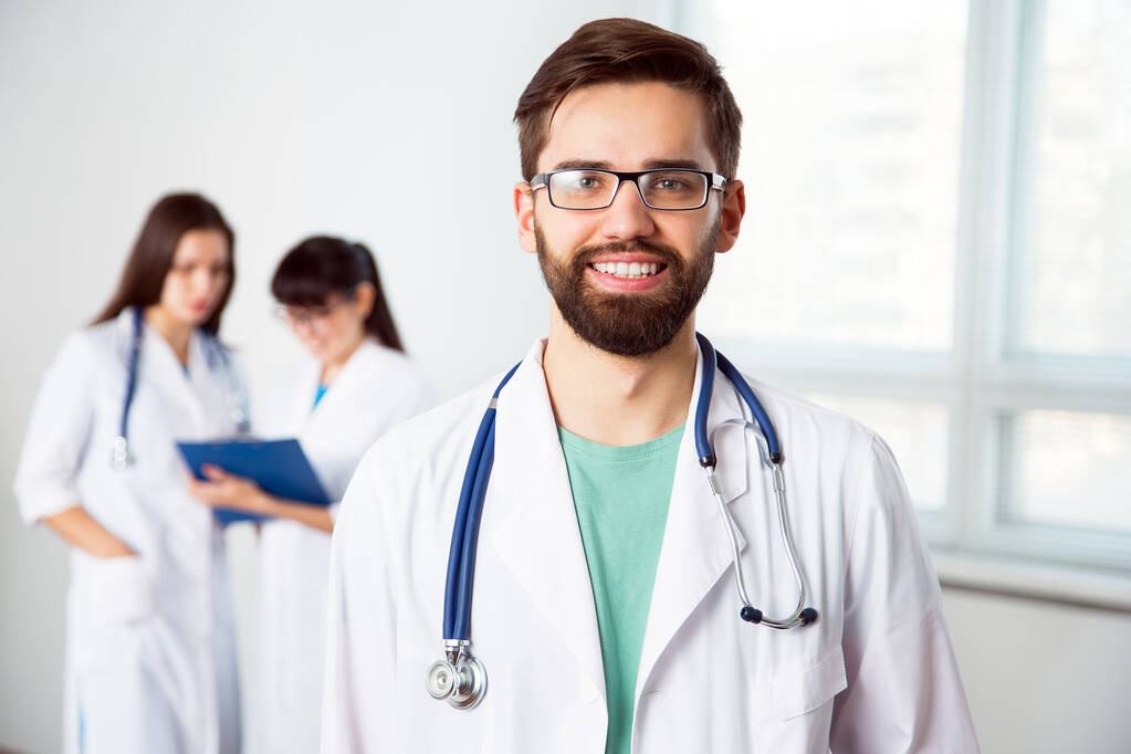Porträt eines jungen Arztes in einer Klinik mit Kollegen im Hintergrund - Foto, Bild