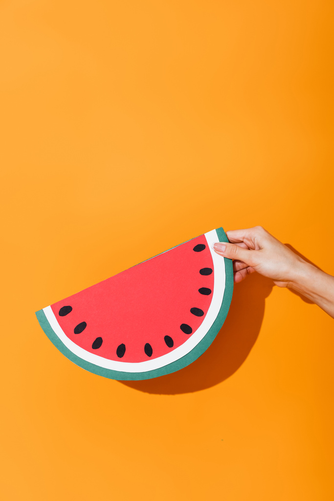 cropped view of girl holding paper cut watermelon on orange - Photo, Image
