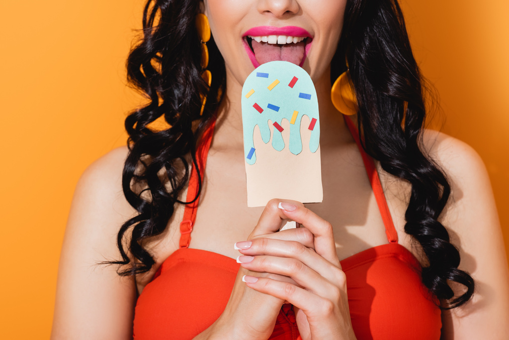 обрізаний вид щасливої молодої жінки, що лиже папір вирізав морозиво на апельсині
  - Фото, зображення