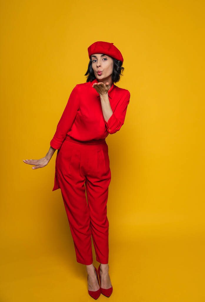 Do u like my look? Full-length photo of a smiley woman on her holiday dressed in a red suit, standing flirtatious, sending an air kiss. - Photo, Image