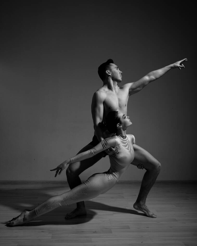 男と女が現代バレエを踊っている。アクロバティックなカップルは白い背景で数字を実行します。サポート付きのパフォーマンスをリハーサルする体操選手のデュエット。モノクロームの写真. - 写真・画像