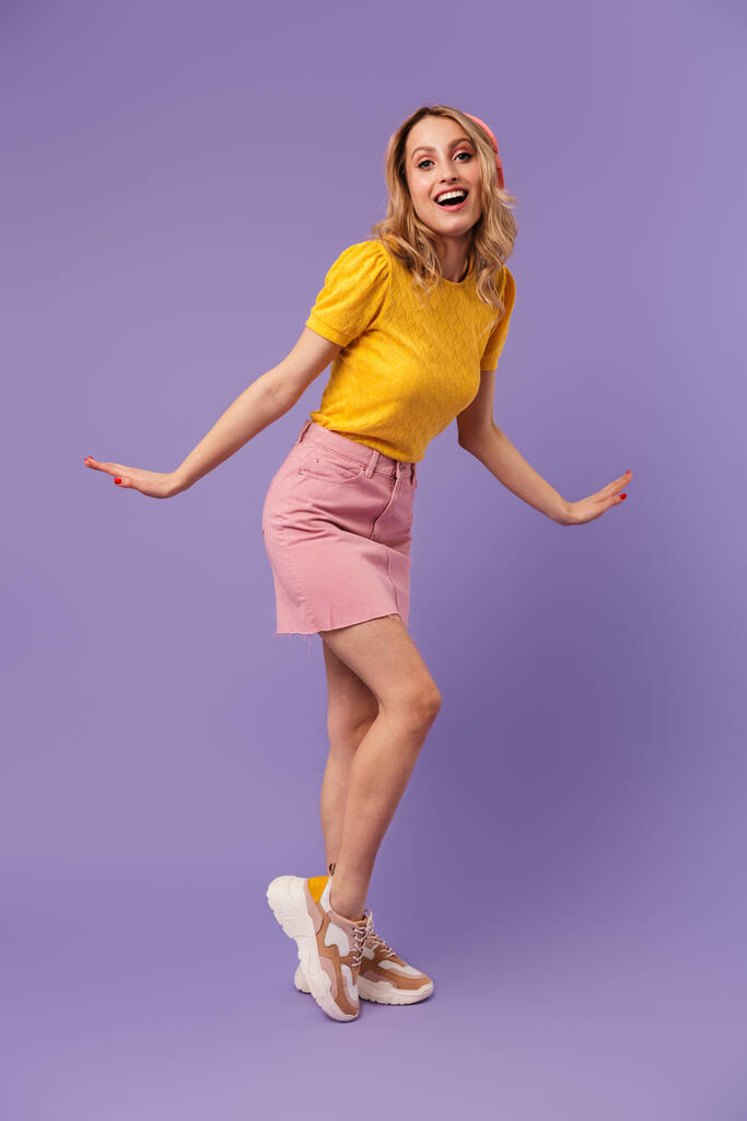 Image de belle femme heureuse dansant et chantant tout en utilisant des écouteurs isolés sur fond violet - Photo, image