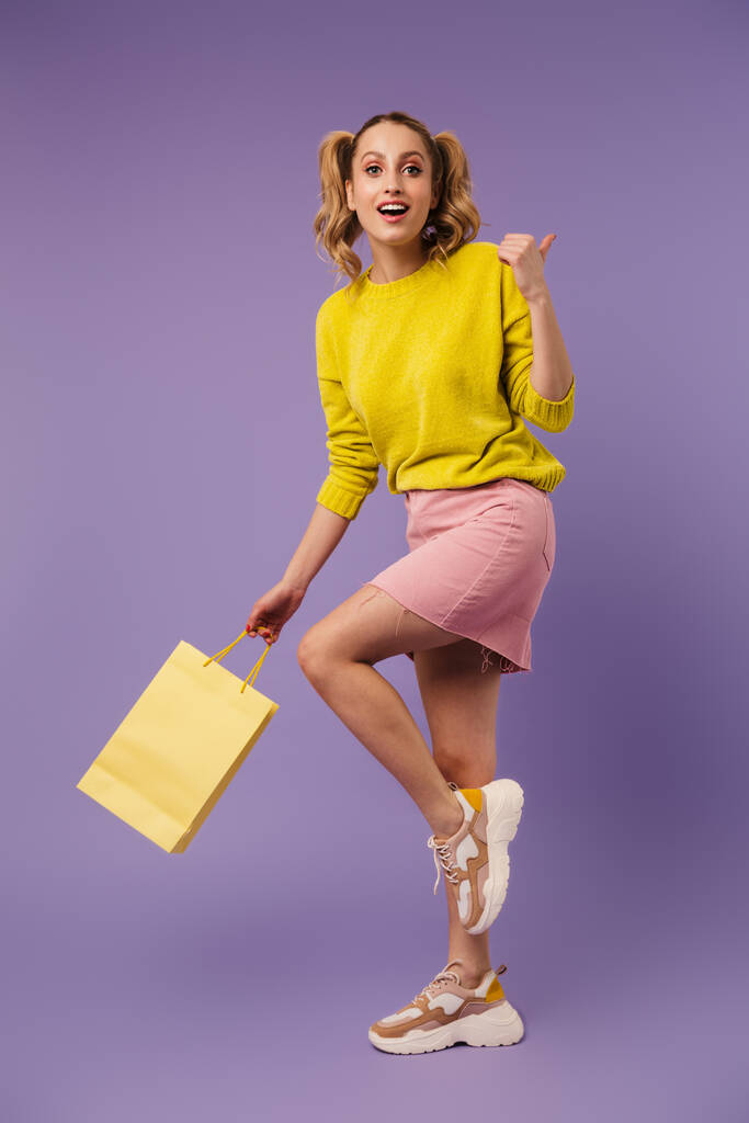 Image of excited pretty woman with shopping bag pointing thumb backward isolated over purple background - Photo, Image