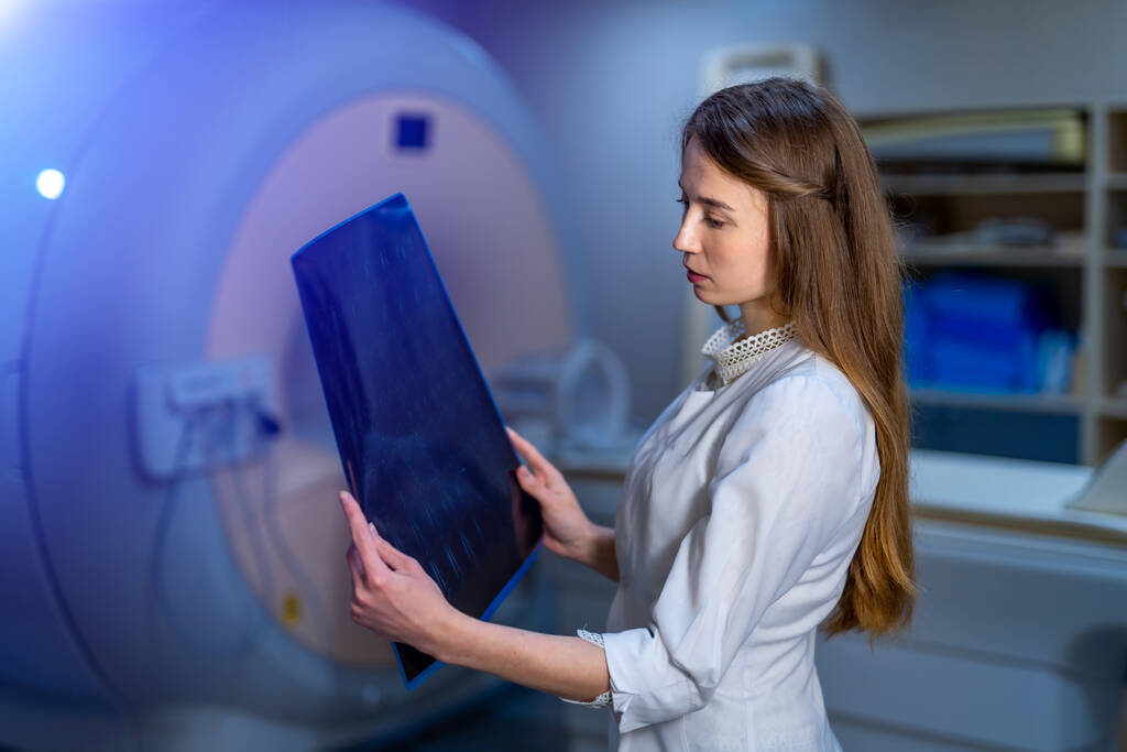 Beautiful female doctor with x-ray in hands. CT machine on background. Radiology. - Photo, Image