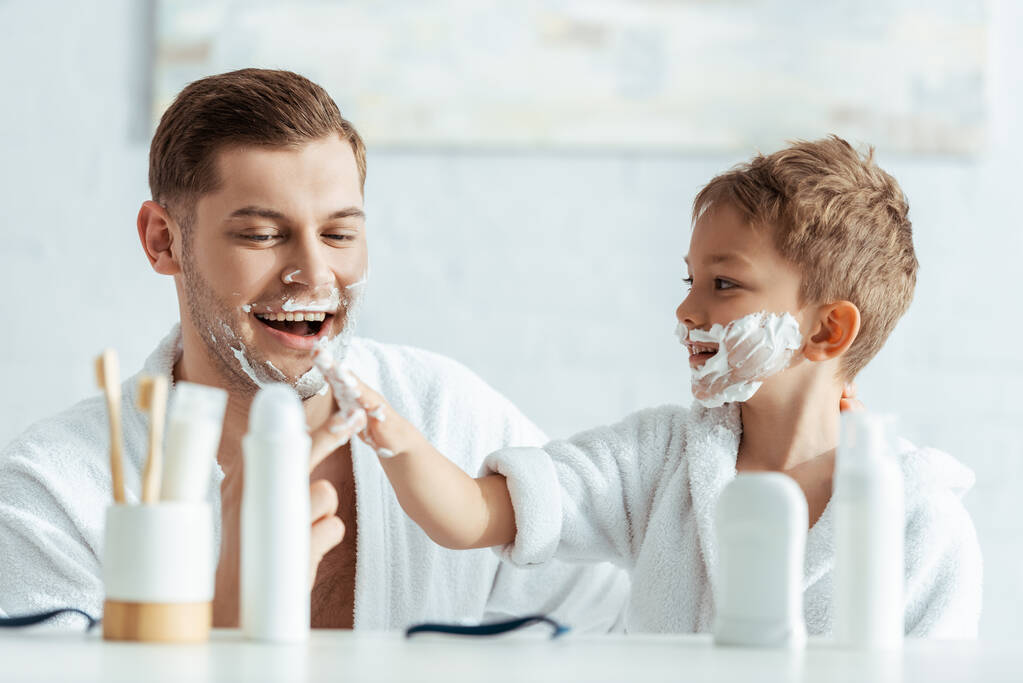 szelektív fókusz mosolygós fiú alkalmazása borotválkozás hab arcát vidám apa - Fotó, kép
