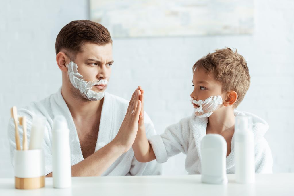 foco seletivo de pai sério e filho com espuma de barbear em rostos dando alta cinco
 - Foto, Imagem