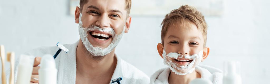 horizontal image of happy father and son with shaving foam on faces holding shaving razors - Photo, Image