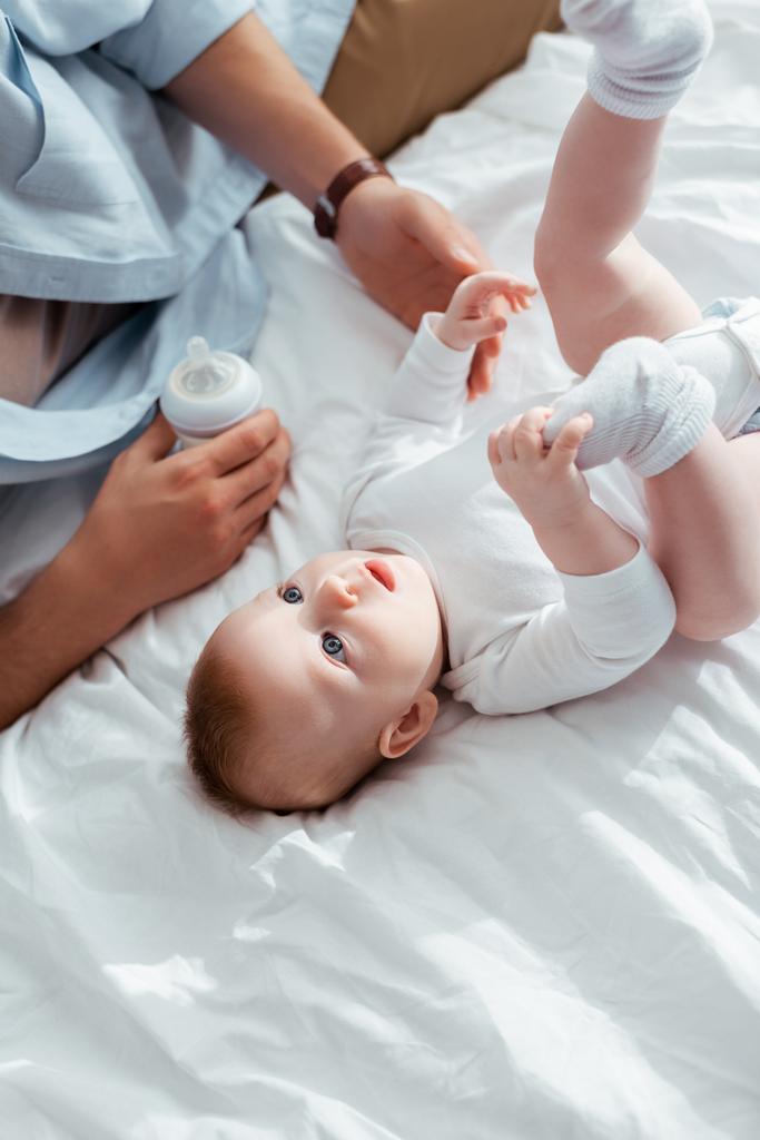 oříznutý pohled na otce drží kojeneckou láhev s mlékem v blízkosti rozkošný malý syn - Fotografie, Obrázek