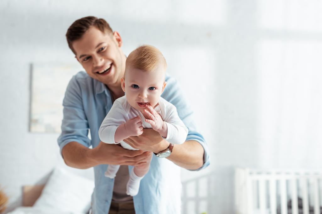 lindo bebé chico mirando cámara en manos de feliz padre
 - Foto, imagen