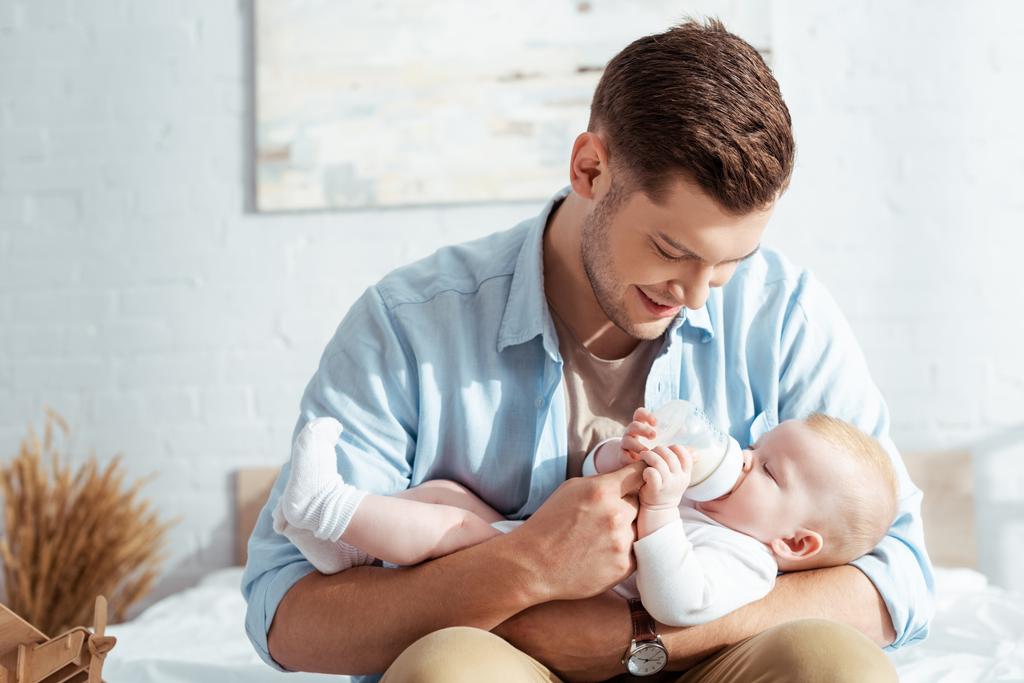 счастливый молодой отец кормит симпатичного мальчика молоком из детской бутылочки
 - Фото, изображение