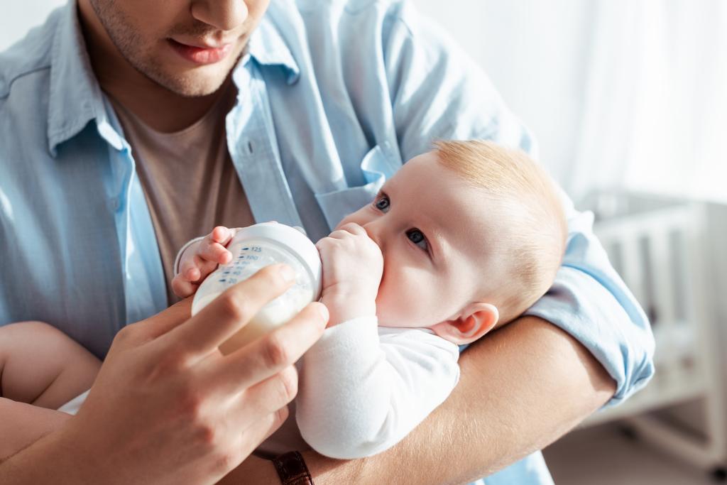 обрізаний вид молодого батька, що годує милого хлопчика молоком з дитячої пляшки
 - Фото, зображення