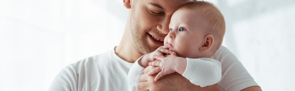 horizontaal beeld van gelukkig vader met gesloten ogen houden kleine baby jongen op handen - Foto, afbeelding