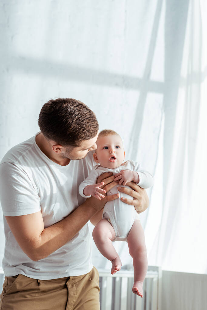 joven padre sosteniendo lindo bebé niño en cuerpo mameluco en manos
 - Foto, imagen