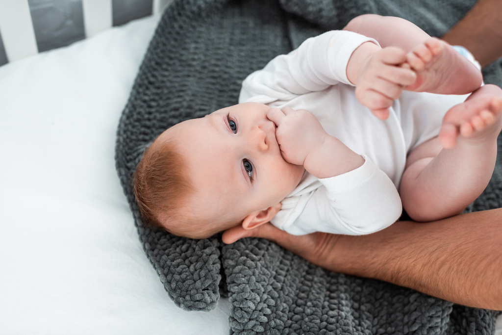 vue recadrée de l'homme touchant adorable bébé couché dans un lit bébé sur une couverture, mise au point sélective - Photo, image