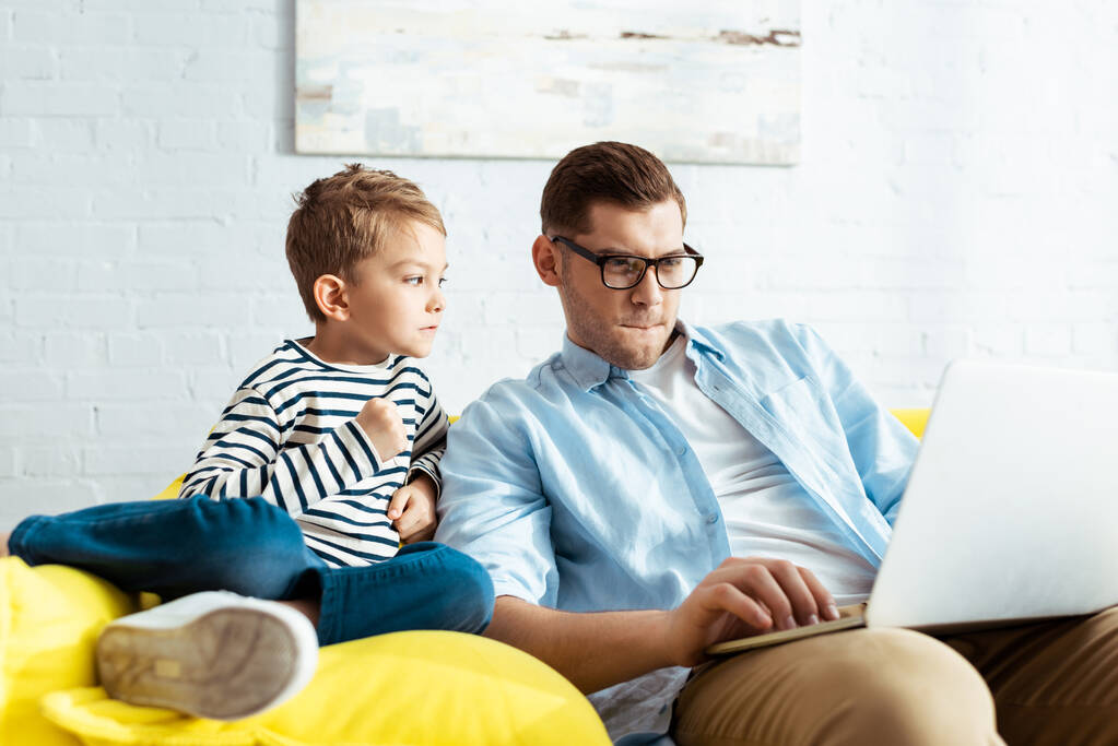 αξιολάτρευτο παιδί κοιτάζει περιποιητικός πατέρας χρησιμοποιώντας φορητό υπολογιστή - Φωτογραφία, εικόνα