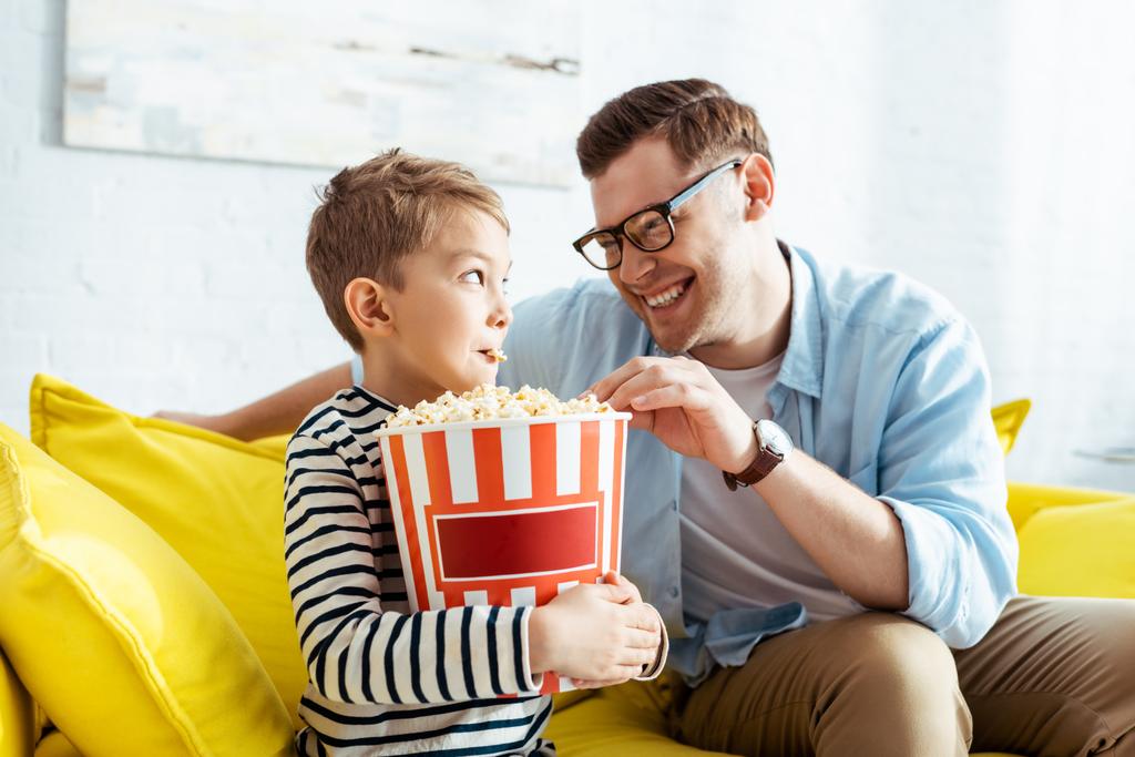 Glücklicher Vater und Sohn schauen sich beim Popcorn-Essen aus Eimer an - Foto, Bild