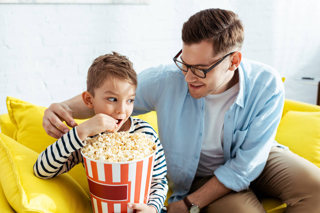 padre felice guardando il figlio mangiare popcorn dal secchio - Foto, immagini