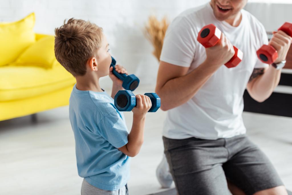 vista recortada del hombre cerca de hijo haciendo ejercicio con pesas en casa
 - Foto, imagen
