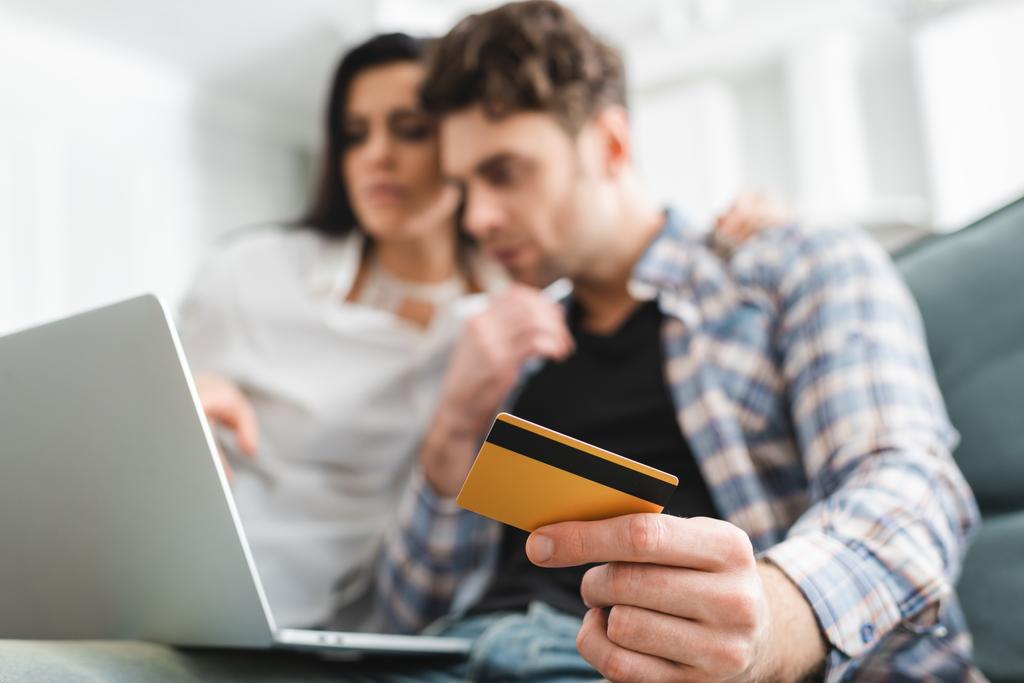Selektiver Fokus des Mannes, der Kreditkarte hält, während er Laptop in der Nähe seiner Freundin benutzt  - Foto, Bild