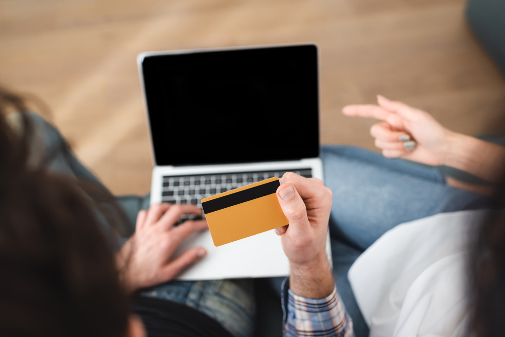 Visão aérea do homem segurando cartão de crédito enquanto namorada apontando com o dedo para laptop
  - Foto, Imagem