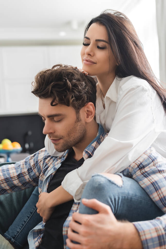 Selective focus of beautiful girl embracing handsome boyfriend with closed eyes at home  - Photo, Image