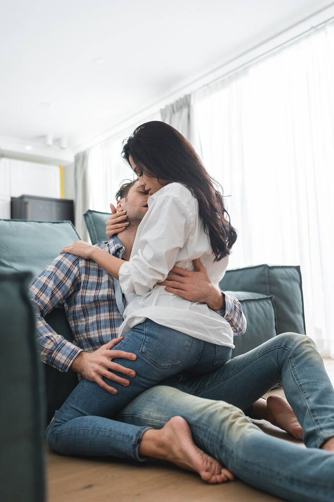 Foco seletivo de mulher sensual abraçando namorado no chão perto do sofá em casa
  - Foto, Imagem